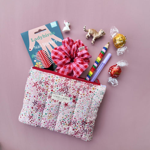 Liberty London fabric star patterned pouch with child gifts and stationary items on a pink background